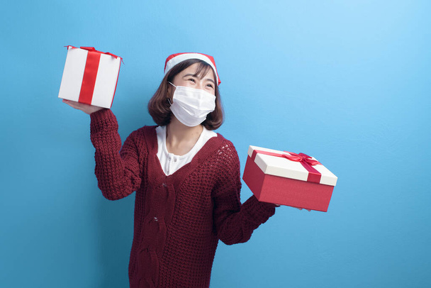 Portrait of young smiling woman in surgical mask wearing red Santa Claus hat isolated blue background studio. - Foto, immagini