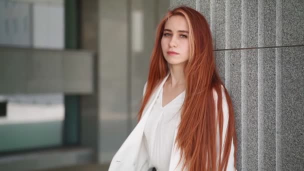 Portrait. Beautiful confident business woman with red hair in fashion clothes stands near the corporate office. Young lady enjoying successful career Elegant female entrepreneur downtown. Slow motion. - Footage, Video