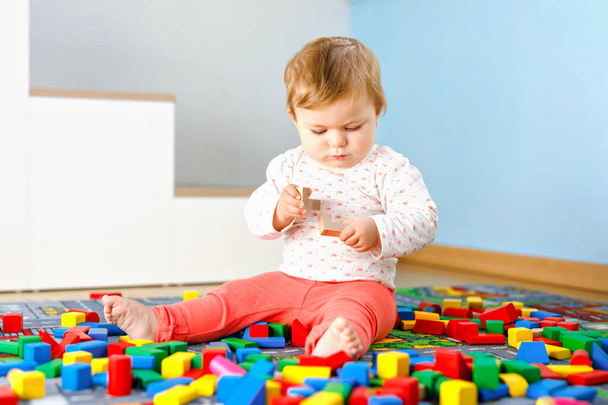 Urocza dziewczynka bawiąca się zabawkami edukacyjnymi. Szczęśliwe zdrowe dziecko bawiące się kolorowe różne drewniane klocki w domu w pokoju domowym. Baby uczenia się kolorów i form - Zdjęcie, obraz