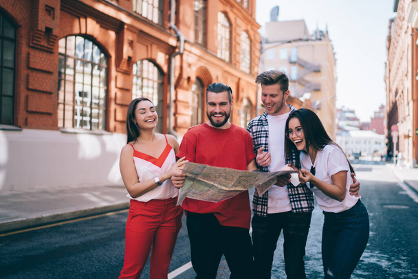 Happy hipster guys in casual clothing using location map for reading navigation information during travel sightseeing, Caucasian male and female discussing trip vacations during walking activity - Foto, immagini