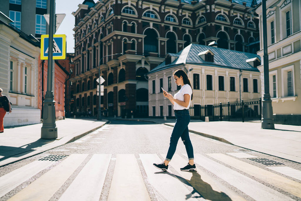 Caucasian female user walking in touristic city connecting to roaming internet for tracking gps during sightseeing, millennial hipster girl exploring town searching online guide on smartphone gadget - Фото, изображение
