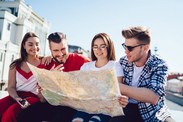 Group of cheerful tourists using travel map for search direction route and explore city during summer vacations, happy Caucasian hipster guys with orientation paper discussing funny journey trip - Фото, изображение