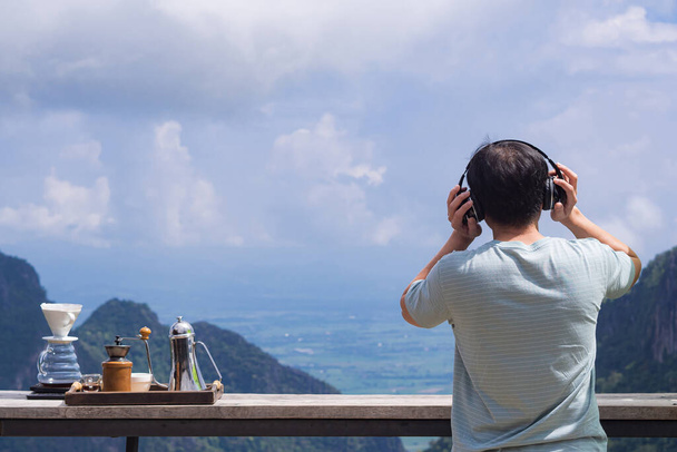 Widok z tyłu człowieka stojącego słuchać ulubionej piosenki ze słuchawką bezprzewodową i cieszyć się patrząc na piękne góry widok. Poczucie szczęścia i wolności. Miejsce na tekst - Zdjęcie, obraz