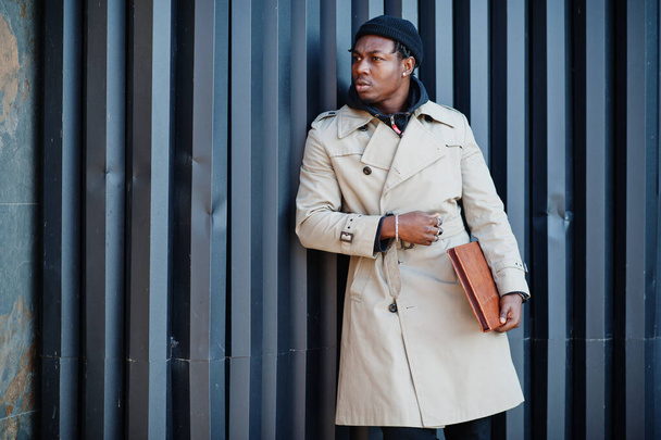 Handsome african american man posing outside in black hat and beige coat with folder in hand. - Foto, Imagem