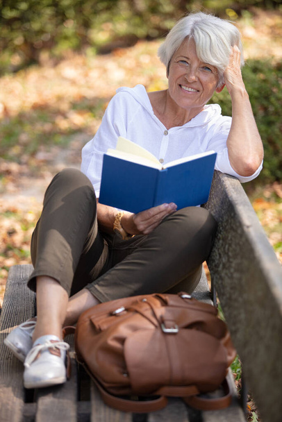 retired woman reading a book on the bench - Фото, изображение