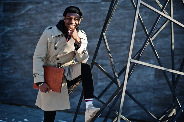 Handsome african american man posing outside in black hat and beige coat with folder in hand. - Zdjęcie, obraz