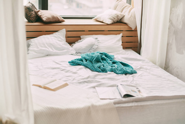 En la cama del dormitorio hay un libro abierto, una manta azul y un montón de almohadas. Mañana temprano, dormitorio de la mañana. - Foto, imagen