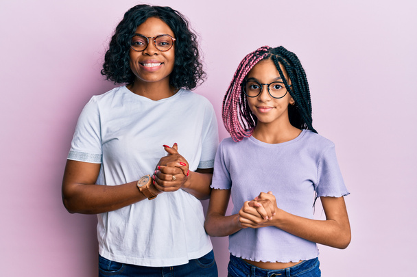 Bella afroamericana madre e figlia indossa abiti casual e occhiali con le mani unite e le dita incrociate sorridenti rilassati e allegri. successo e ottimismo  - Foto, immagini