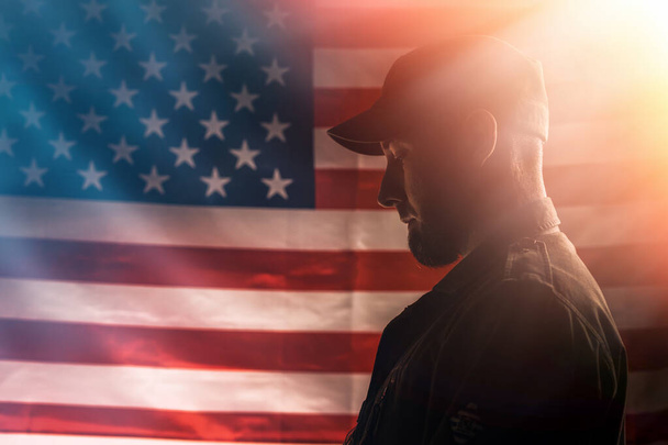 Memorial day. A uniformed soldier stands in sadness against the backdrop of the American flag. Copy space. Side view. The concept of the American national holidays and patriotism. - Photo, Image