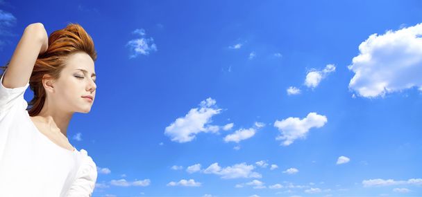 Portrait of red-haired girl in white on blue sky background. - Photo, image