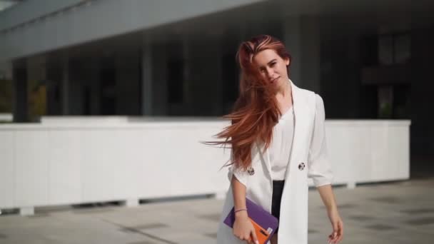 Beautiful confident business woman with red hair in fashion clothes smiles and rejoices. Lady enjoying successful corporate career. Female entrepreneur spinning with happiness downtown. Slow motion. - Footage, Video