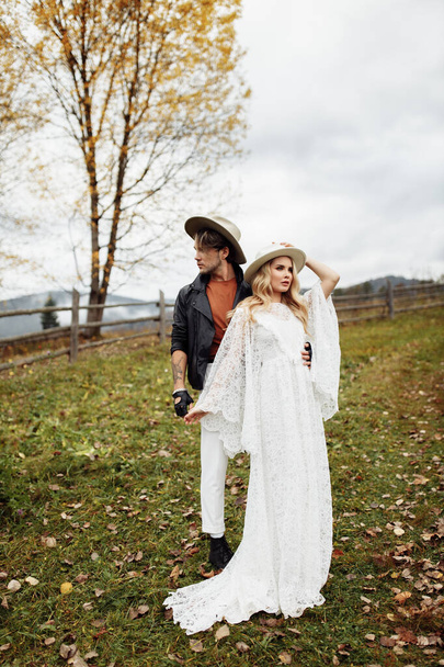 Handsome man and beautiful woman walking at the field, wearing hats, enjoy weekend together, loving husband gently hold a hand of adorable wife, fashionable couple concept. High quality photo - Foto, afbeelding