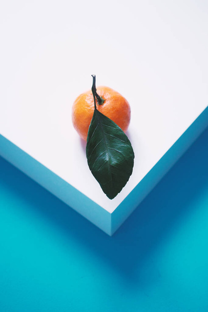 One fresh tangerine with leaves lies on a blue wooden table. Vertical photo with empty space on top for text - Φωτογραφία, εικόνα