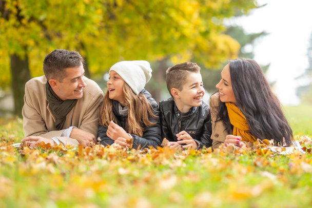 Happy family having conversation on a blanket outdoors with parents chatting with their children in the autumn. - Photo, Image