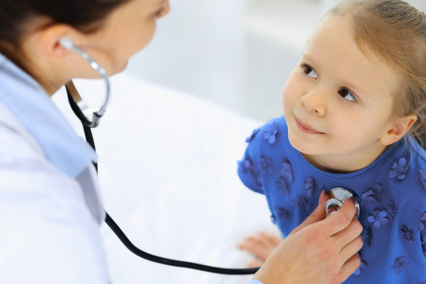 Doctor examining a little girl by stethoscope. Happy smiling child patient at usual medical inspection. Medicine and healthcare concepts - Foto, Bild