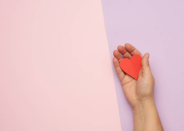 mano femenina sosteniendo el corazón de papel rojo sobre un fondo rosa, vista superior, espacio para copiar - Foto, imagen