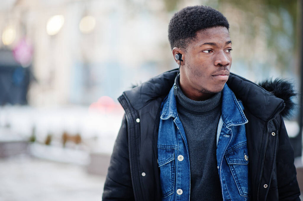 El hombre africano usa chaqueta en invierno frío posó al aire libre con auriculares en las orejas. - Foto, Imagen