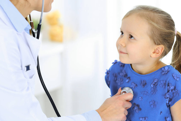 Dokter die een klein meisje onderzoekt met stethoscoop. Gelukkige glimlachende kindpatiënt bij gebruikelijke medische inspectie. Begrippen geneeskunde en gezondheidszorg - Foto, afbeelding