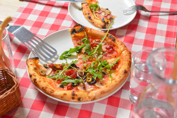 Supreme pizza on a white plate over red plaid tablecloth. Italian cuisine, Italian concept. Still life, eating Italian pizza in restaurant or diner. Eating out concept. - Photo, image