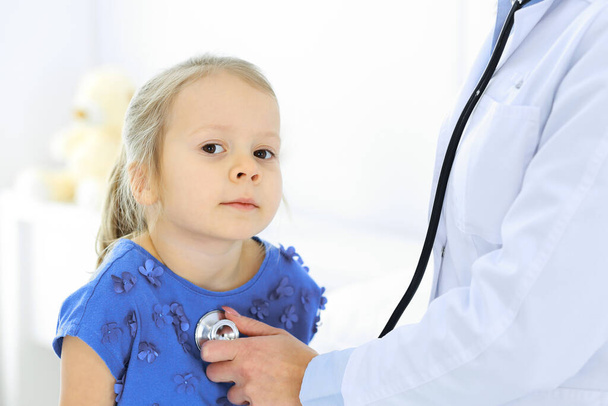 Doktor vyšetřuje malou holčičku stetoskopem. Šťastný usměvavý dětský pacient při běžné lékařské prohlídce. Medicína a zdravotní koncepce - Fotografie, Obrázek