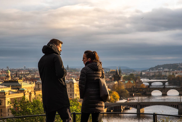 Homme et femme marchent et parlent sur le parc Letna tout en ayant une vue spectaculaire sur le centre-ville à l'automne 2020 sur Prague 6, pendant la période de quarantaine en raison de l'épidémie de COVID-19 que l'hiver commence, République tchèque - Photo, image