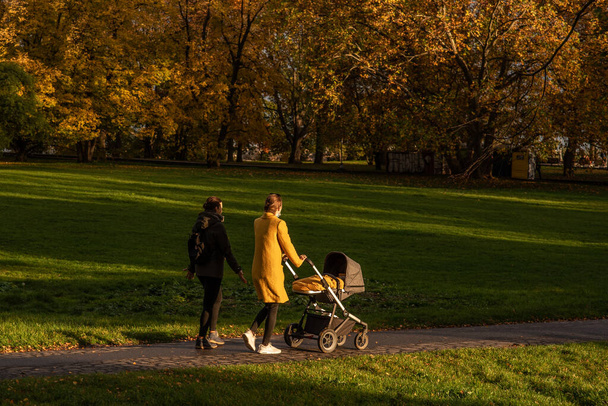 Duas mulheres (uma carregando um bebê passear) estão desfrutando de um passeio Outono 2020 em Praga 6, durante o período de quarentena devido ao surto de COVID-19 como o inverno está começando, República Checa - Foto, Imagem