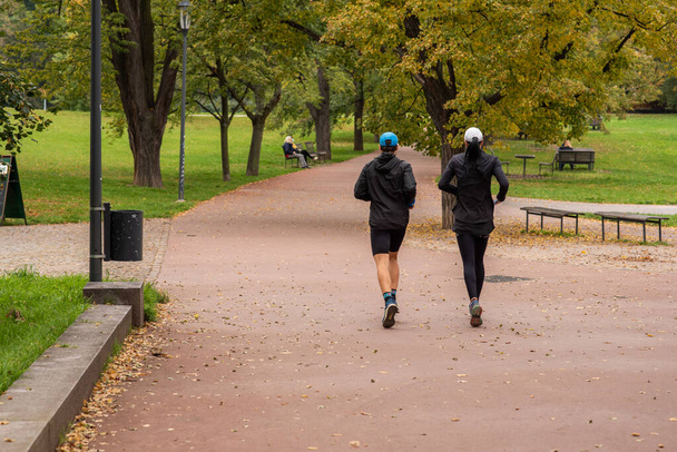 Man and woman are running and talking on Letna Park in Autumn 2020 on Prague 6, during quarantine period due to outbreak of COVID-19 as winter is starting, Czech Republic - Photo, Image