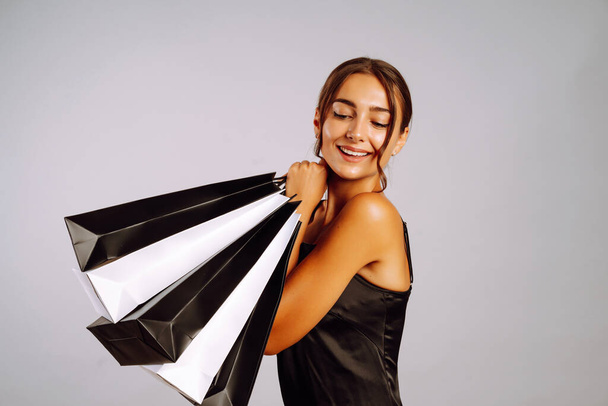 Fashion woman in black dress with shopping bags posing on grey background.  Black friday, sale, consumerist, lifestyle concept. - Foto, immagini