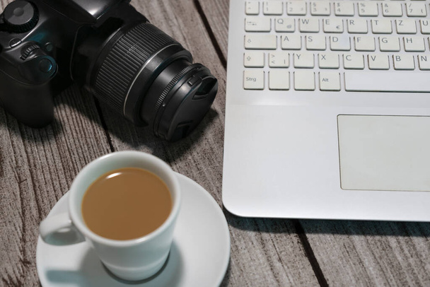 Scrivania da lavoro per fotografi vista dall'alto, con fotocamera, computer portatile e una tazza di caffè. - Foto, immagini