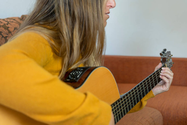 家庭で西洋のアコースティックギターを弾く若い女の子。ライフスタイル音楽とエンターテイメントのコンセプト. - 写真・画像