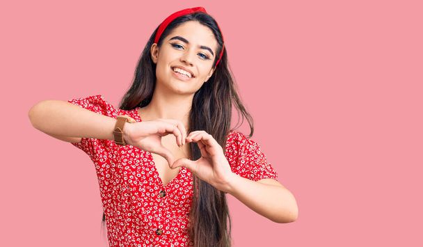 Brunette teenager girl wearing summer dress smiling in love doing heart symbol shape with hands. romantic concept.  - Photo, Image