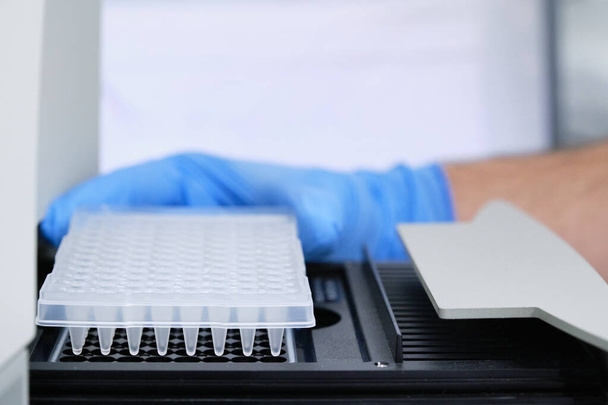 Een onderzoeker zet PCR plaat op de thermische cycler voor DNA versterking. PCR-test met coronavirus. - Foto, afbeelding