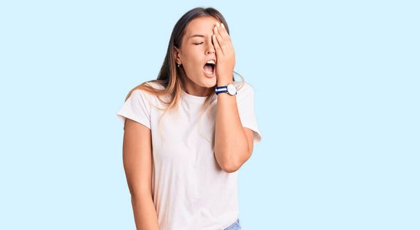 Beautiful caucasian woman wearing casual white tshirt yawning tired covering half face, eye and mouth with hand. face hurts in pain.  - Photo, Image