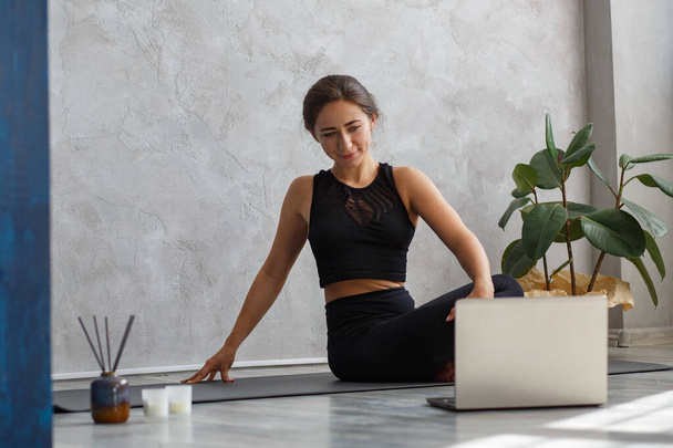 Young sporty woman watching online yoga lessons on laptop. Beautiful girl practicing Lord of the Fishes pose. Yoga postures, meditation, relaxation, stress management, wellbeing and health - Foto, Imagem