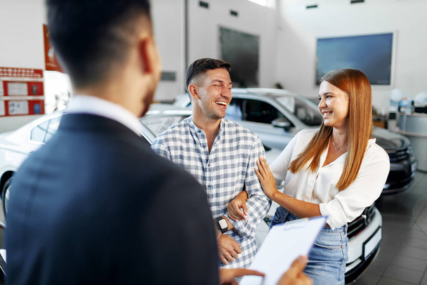 Man car salesman telling about the features of the new car to the couple - 写真・画像