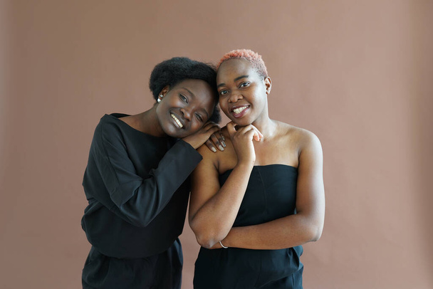 Dvě krásné afroamerické mladé dívky objímající na hnědém pozadí. - Fotografie, Obrázek