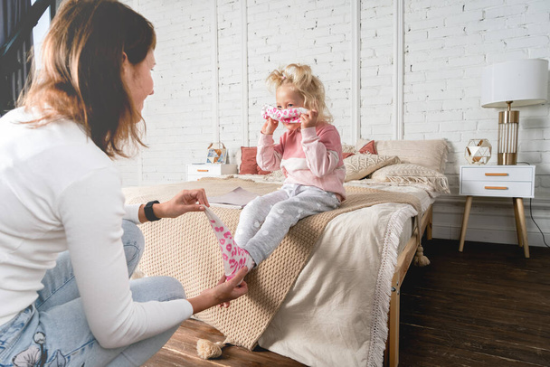 Mom takes off her little daughters socks and tickles her feet a little. The girl laughs. - Photo, image