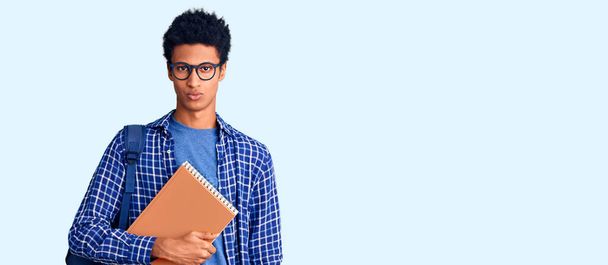 Mladý africký Američan, oblečený do studentského batohu, drží knihu skeptickou a nervózní a mračí se kvůli problému. negativní osoba.  - Fotografie, Obrázek