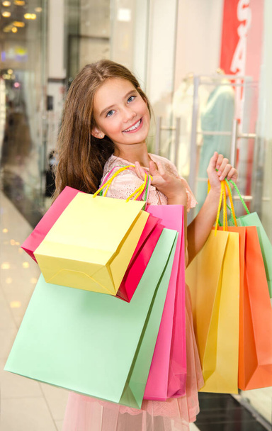 Beautiful happy smiling little girl child is holding shopping bags in shopping mall. Preteen teenager in shopping. Lifestyle concept - Zdjęcie, obraz