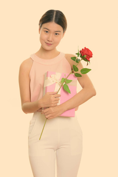 Young beautiful Asian woman holding red rose and gift box ready for Valentines day - Foto, Bild