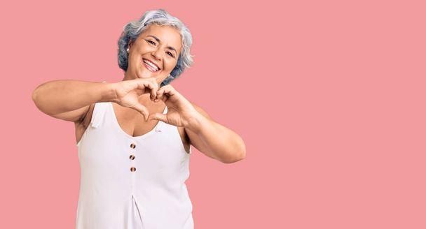 Seniorin mit grauen Haaren in lässiger Kleidung, verliebt lächelnd und in Herzform mit Händen. Romantisches Konzept.  - Foto, Bild