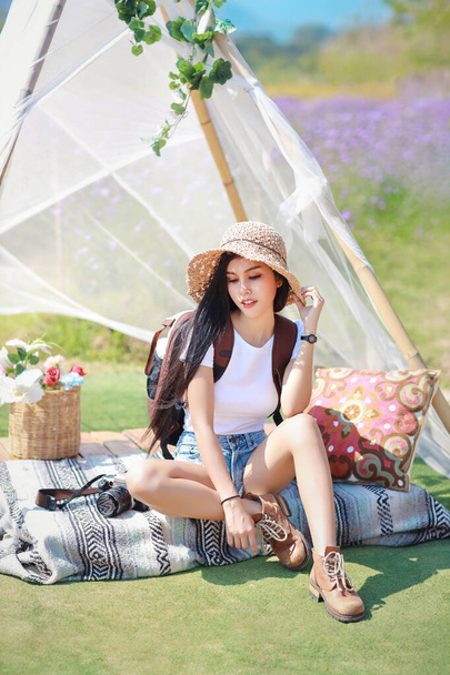 Азиатская красивая женщина, длинные волосы в белой рубашке с камерой и шляпой, сидящей на Вербене с голубым небом. Портрет милая девушка наслаждается среди цветочной фермы. Концепция путешествия на природе - Фото, изображение