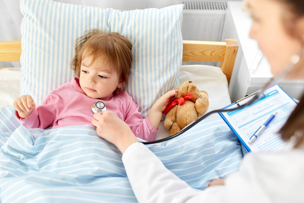 doctor with stethoscope and sick girl in bed - Foto, imagen
