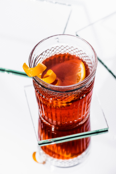 vysoký úhel pohledu na pomerančovou kůru ve skle s alkoholovým koktejlem na bílém povrchu - Fotografie, Obrázek
