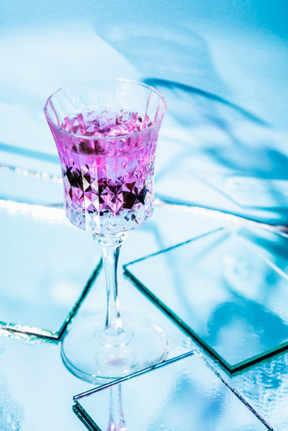 purple alcohol cocktail in glass near mirrors on surface and blue background  - Foto, Imagem