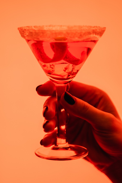 close up of margarita cocktail with ice cubes in female hand on orange - Photo, Image