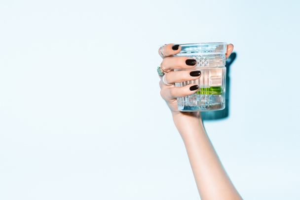 bijgesneden uitzicht op jonge vrouw met glas met limoen in alcohol drinken op blauw - Foto, afbeelding