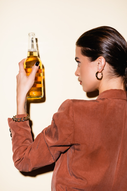 brunette woman in brown blazer looking at bottle with beer on white - Foto, Imagem
