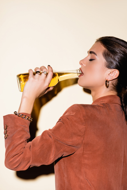 side view of brunette woman in brown blazer drinking beer on white - Foto, Imagem