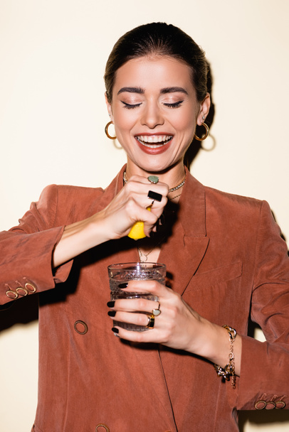 happy woman in brown blazer squeezing lemon in glass with alcohol cocktail on white  - Foto, imagen